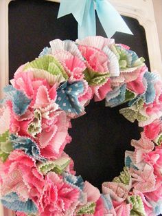 a pink and blue wreath on a black door with a bow hanging from it's side