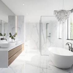 a bathroom with marble walls and flooring, white bathtub next to two sinks under a crystal chandelier