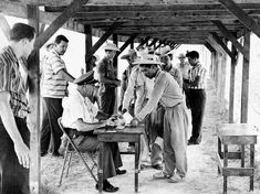 a group of men standing around a table with papers on it and one man wearing a straw hat