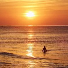 a person sitting in the ocean at sunset