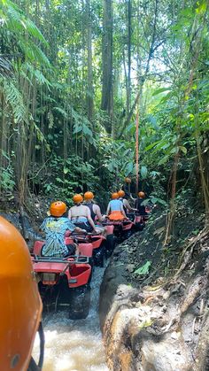 four people are riding atvs down a muddy stream in the jungle with helmets on their heads