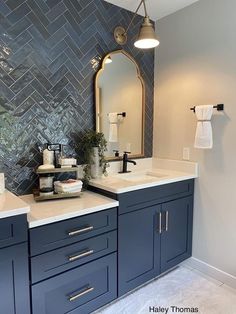 a bathroom with two sinks and a mirror on the wall next to it is decorated in gray herringbone tile