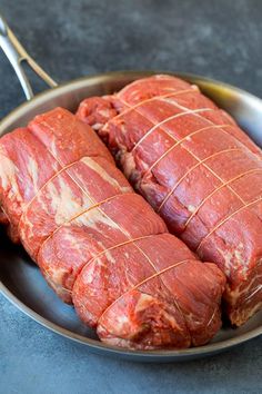 two pieces of raw meat in a pan with tongs on the side and fork