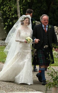 the bride and groom are walking down the path together in their kilts, dressed in traditional scottish garb