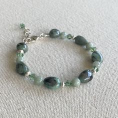 An earthy, yet elegant bracelet with vivid Emerald hues reminiscent of the lush, verdant landscapes of Ireland. It is made with stormy Green Emerald nuggets, soft Green Jade and sparkling Green crystals. It is accented with gleaming sterling silver saucer beads and findings to add a refined look to the natural gemstones. It is finished with a lobster claw clasp and extension chain that makes it easy to put on and adjustable to fit wrists 7 1/2" - 8 1/2". Elegant Green Faceted Bead Bracelet, Green Glass Bracelets With Faceted Beads, Green Hand-strung Crystal Bracelet, Hand-strung Green Jade Beaded Bracelets, Bracelet Emerald, Green Faceted Artisan Beads, Nugget Bracelet, Emerald Isle, Elegant Bracelet