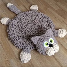 a crocheted cat rug is laying on the floor with eyes wide open and it's tail curled up