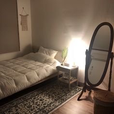 a bed sitting next to a mirror on top of a wooden floor in a room