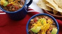 two blue bowls filled with chili and cheese next to tortilla chips on a red towel