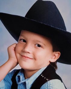 a young boy wearing a black cowboy hat and posing for a photo with his hand on his chin