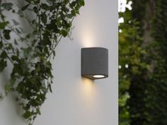 an outdoor wall light mounted on the side of a white building with greenery in the background