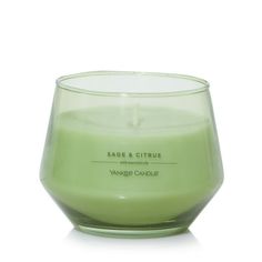 a green candle sitting on top of a white table next to a glass container filled with liquid