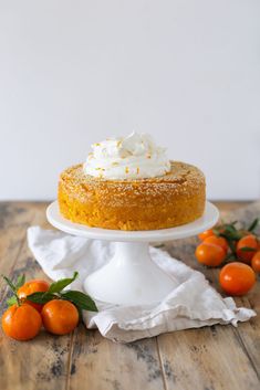 a cake sitting on top of a wooden table next to oranges and whipped cream