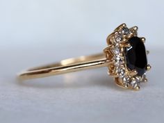 a gold ring with an oval cut black diamond surrounded by smaller round white diamonds on the band