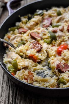 a skillet filled with rice and vegetables on top of a wooden table next to a fork