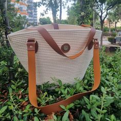 a white and brown bag sitting on top of green plants in the grass with trees behind it