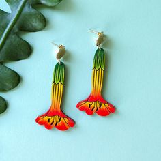 a pair of colorful bird shaped earrings sitting on top of a table next to a plant