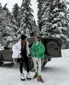 two women standing in the snow next to a jeep