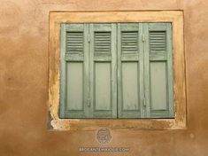 an old window with green shutters on the side of a tan colored building,