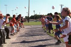 a group of children are throwing balls in the air on a street lined with grass