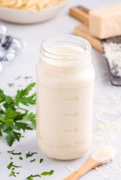 a glass jar filled with white liquid next to some parsley and other food items