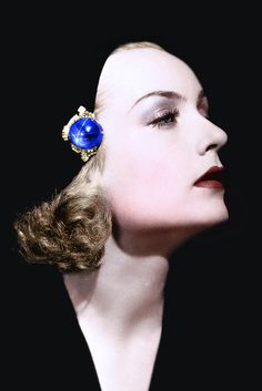 a woman with her head tilted to the side wearing a pair of blue and gold earrings