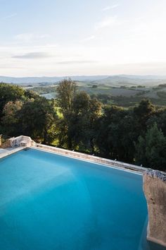 an empty swimming pool in the middle of a lush green field with trees and rolling hills