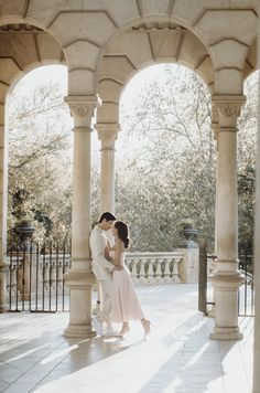 a man and woman are kissing under an arch in the middle of a walkway with columns