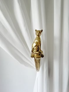 a gold cat statue sitting on top of a white curtain with the curtains pulled back