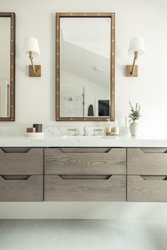 a bathroom vanity with two mirrors and lights on it's sides, in front of a white tiled floor