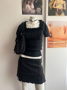 a mannequin wearing a skirt and sweater with pictures on the wall behind it