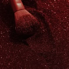 a red brush sitting on top of a floor covered in glittery dust with the tip of it's bristles sticking out