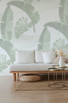 a white couch sitting on top of a wooden floor next to a wall covered in green leaves