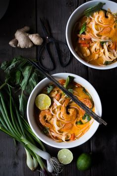 two bowls filled with noodles and vegetables on top of a wooden table next to some chopsticks