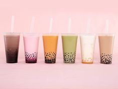 five different colored cups with straws lined up in a row on a pink background