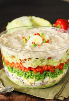 a layered salad in a glass bowl on top of a wooden table with spoons