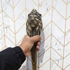 a hand holding a golden lion door handle on a white marble tiled bathroom wall with gold hexagonal tiles