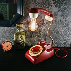 an old fashioned red telephone sitting on top of a table next to a lamp and clock