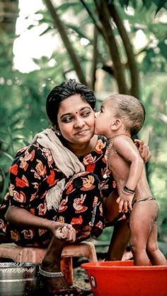 a woman holding a baby in her lap while sitting on top of a red bucket