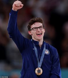 a man with glasses and a medal in his hand is smiling at the camera while he holds up his fist