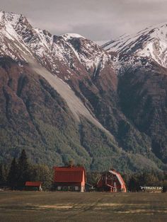 the mountains are covered in snow and there is a red barn on the far side