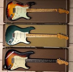 three electric guitars are lined up in a case on the floor next to each other