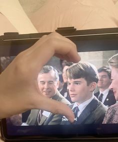 a hand is pointing at a television screen with people in suits and ties on it