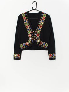 Vintage black beaded cardigan with stunning multi-coloured faux jewels. This beautiful cardigan is in a deep black with faux jewels in blue, red and green and gold beads around the cuffs and down the opening. A stunning piece that will level up any outfit! Made from a soft, lightweight material.  Our recommended size: Medium  Label says: No label  Condition: Very good  Material: 70% acrylic, 30% wool  Measurements in inches: Pit to pit: 19 Shoulders: 16 Front length: 18.5 Back length: 19 Sleeve Embellished Fitted Cardigan For Party, Black Embellished Cardigan For Party, Black Embellished Cardigan For Winter, Winter Multicolor Embroidered Cardigan, Embellished Black Cardigan For Winter, Elegant Embellished Black Cardigan, Vintage Multicolor Cardigan With Buttons, Vintage Multicolor Cardigan, Black Embellished Winter Cardigan