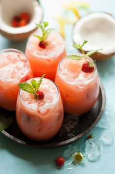 three glasses filled with watermelon and strawberries on a plate next to coconuts