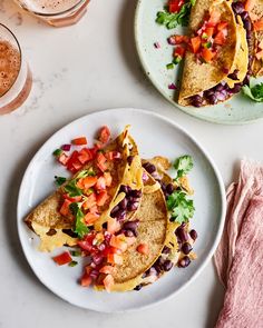 two plates filled with tacos and salsa on top of a white table next to drinks