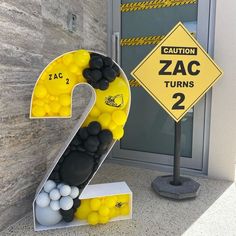 the number two is made out of balloons in front of a sign that says caution zac turns 2