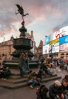 many people are sitting on the ground near a fountain with a statue in the middle