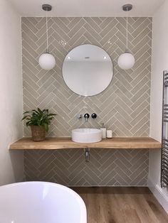 a white sink sitting under a mirror next to a bath tub in a bathroom on top of a wooden floor