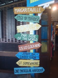 there are many signs on the pole in front of a building that says margaritaville edge of paradise, far side of the world, port of the clock, port of indecion, port of immersion, st