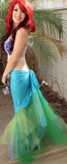 a woman with red hair is dressed in a green and blue mermaid tail skirt as she poses for the camera